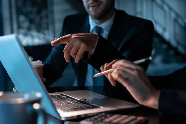 Professional businessman in strategic consultation, gesturing while working on laptop in modern office setting